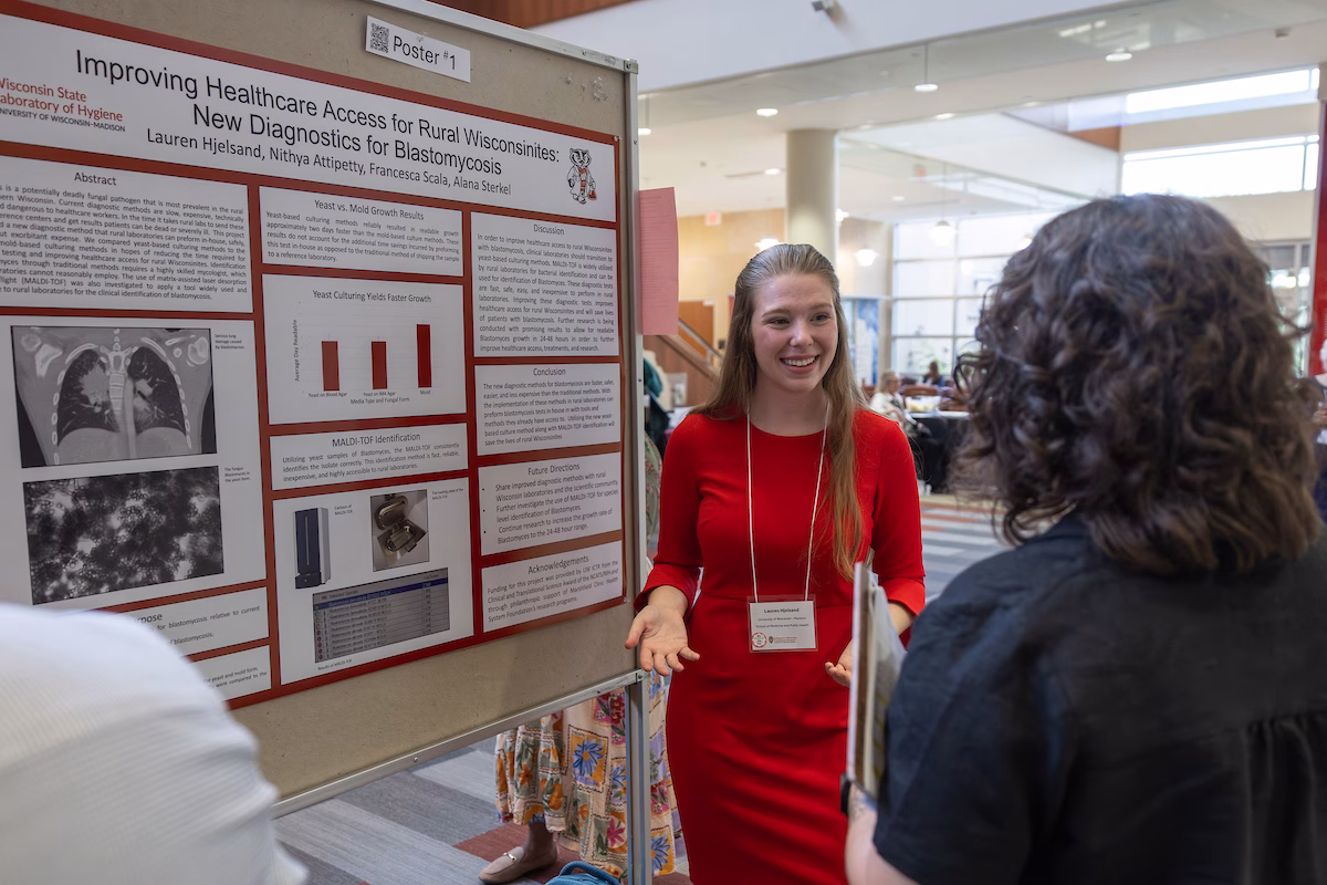 A woman standing in front of a scientific poster describes her work to another event participant.