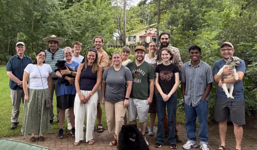 Group of people and dogs smiling at the camera in a backyard with green trees.
